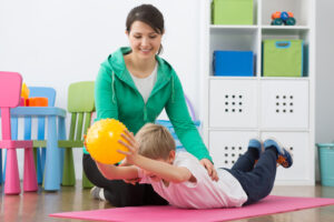 Boy exercising with small gym ball and his smiling instructor